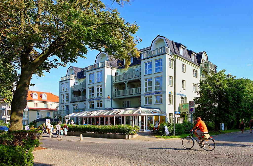 eine Person, die vor einem großen Gebäude Fahrrad fährt in der Unterkunft Am Weststrand Aparthotel Kühlungsborn in Kühlungsborn