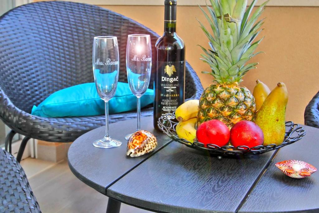 a table with a bowl of fruit and two wine glasses at Bacan Family Apartments in Cavtat
