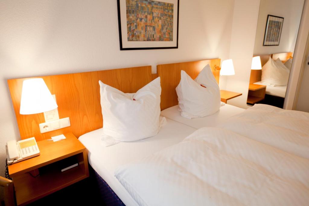 a hotel room with a bed with white sheets and pillows at Hotel Möhringer Hof in Stuttgart