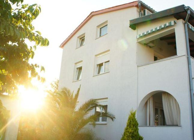 Un grand bâtiment blanc avec le soleil brillant derrière lui dans l'établissement Apartments Vera, à Fažana