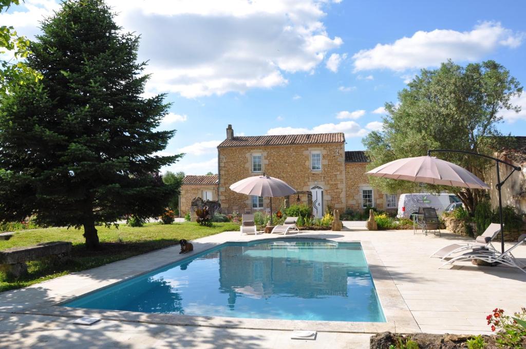 a swimming pool in front of a house with umbrellas at B&B Clos San Gianni in Pujols-sur-Ciron