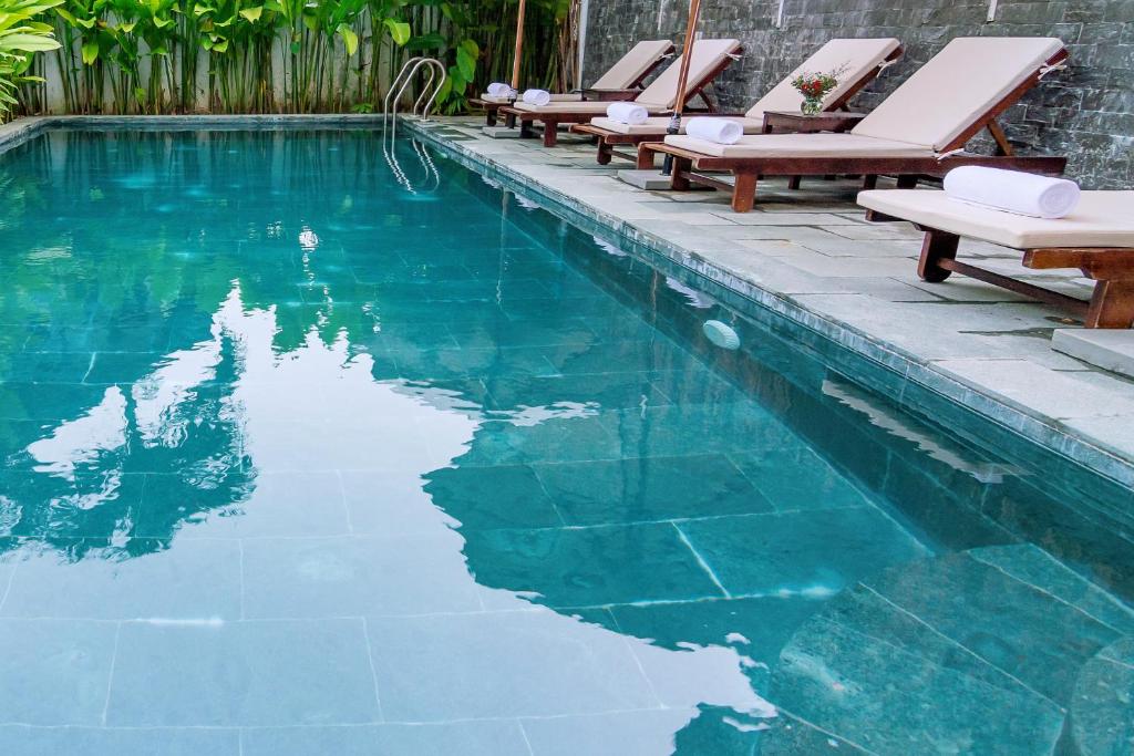 a swimming pool with chairs and blue water at An Bang Beach Villa in Hoi An