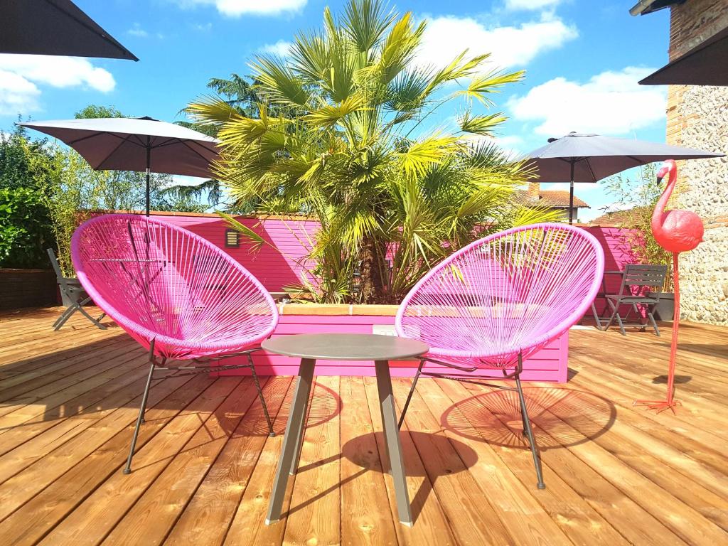 two pink chairs and a table on a deck with umbrellas at Les Granges de Jules in Lafitte-Vigordanne