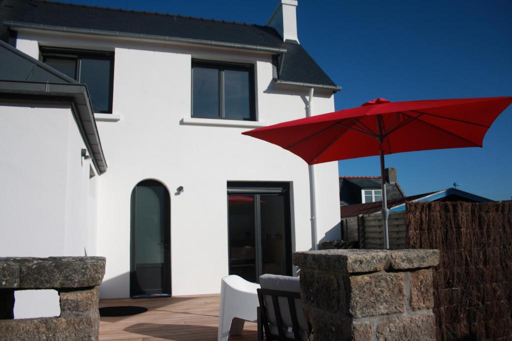 een wit huis met een rode parasol en stoelen bij Maison de Poul Briel in Saint-Guénolé