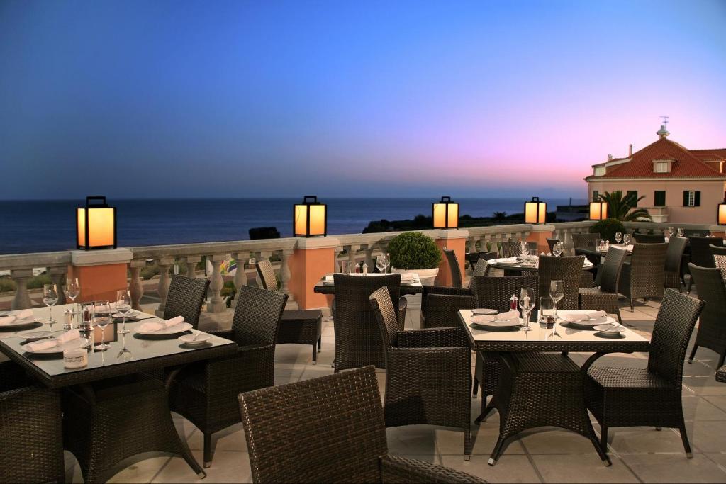 a restaurant with tables and chairs on a balcony with the ocean at Grande Real Villa Itália Hotel & Spa in Cascais