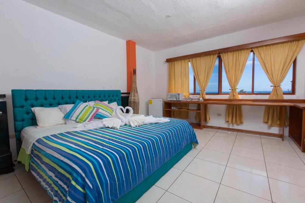 1 dormitorio con 1 cama con cabecero azul y ventanas en Hostal Tongo Reef, en Puerto Baquerizo Moreno