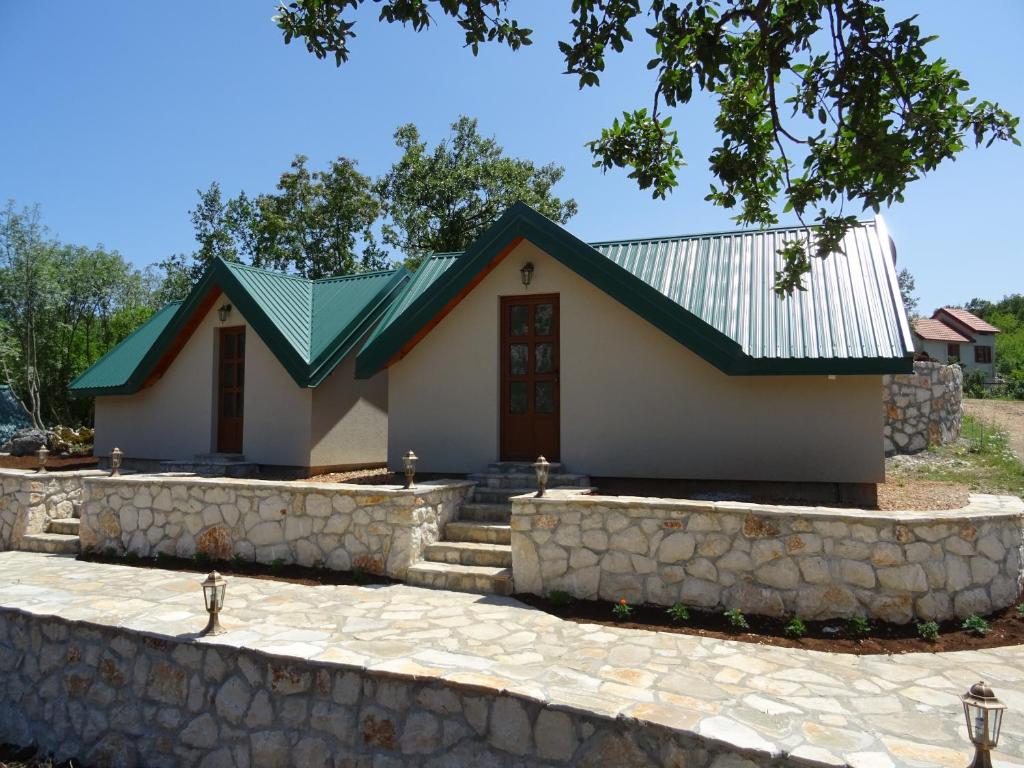 une petite maison blanche avec un toit vert et un mur en pierre dans l'établissement Apartmani Vinici, à Danilovgrad