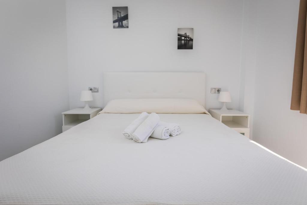 a white bedroom with two towels on a bed at Apartamentos Las Rosas de Capistrano in Nerja