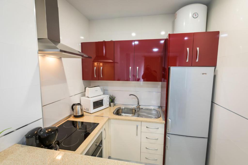 a small kitchen with red cabinets and a white refrigerator at Apartamentos Las Rosas de Capistrano in Nerja