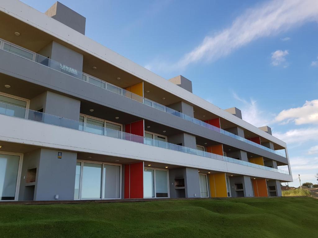 a white building with colorful windows and a green field at Meca Playa in Villa Gesell