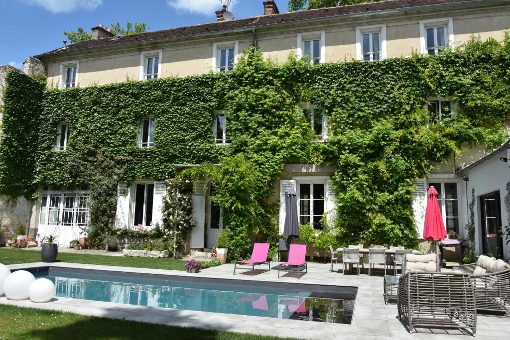 un bâtiment recouvert de lierre avec une piscine et des chaises roses dans l'établissement Demeure Les Aiglons, Chambres d'hôtes & Spa, à Fontainebleau