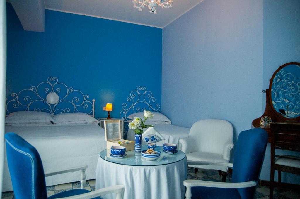 a blue room with a bed and a table and chairs at Hotel Palladio in Giardini Naxos