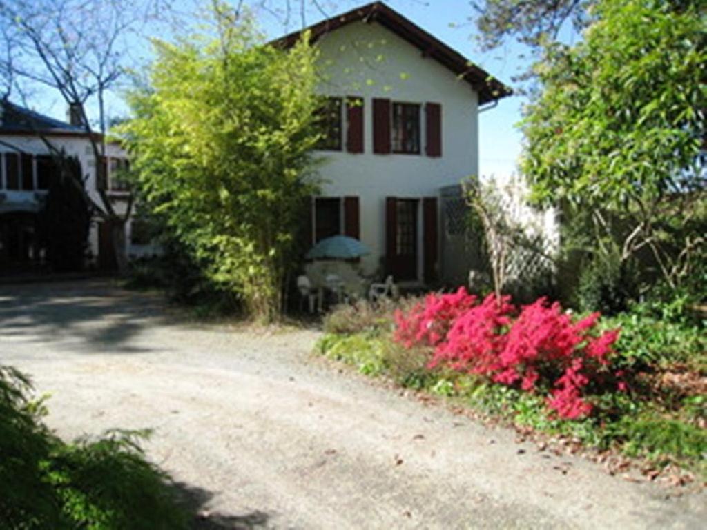 une maison avec des fleurs roses devant un chemin de terre dans l'établissement Appartement La Bananeraie, à Salies-de-Béarn