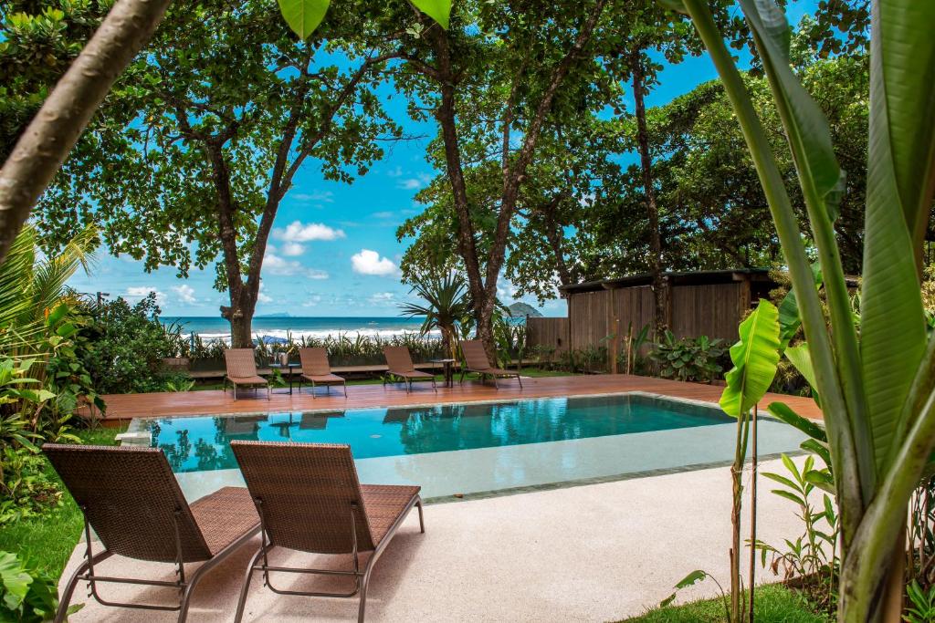 a swimming pool with chairs and the ocean in the background at Flat Pitanga in Camburi