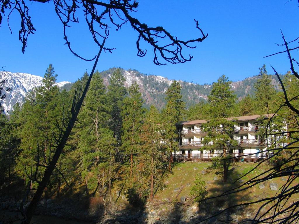 a building in the middle of a forest with mountains at Alpine Rivers Inn in Leavenworth