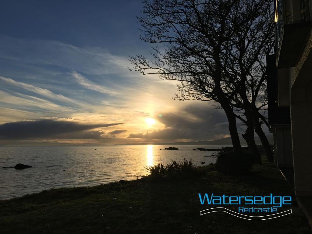 a sunset over a body of water with a tree at Watersedge Redcastle in Red Castle