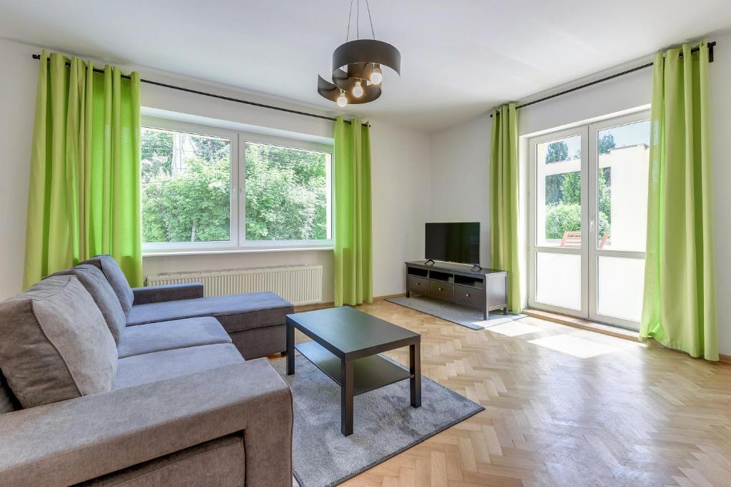 グディニャにあるGdynia Comfort Apartments Perkunaのリビングルーム(緑のカーテン、ソファ、テレビ付)