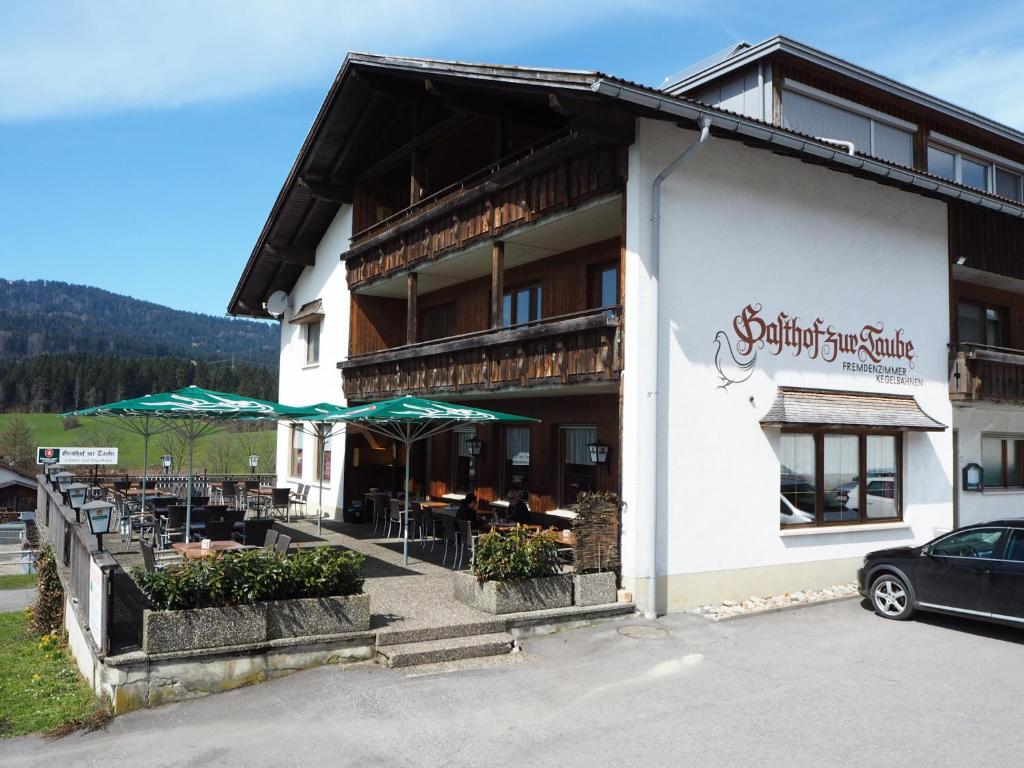 a building with tables and umbrellas outside of it at Pension & Gasthof zur Taube in Sulzberg