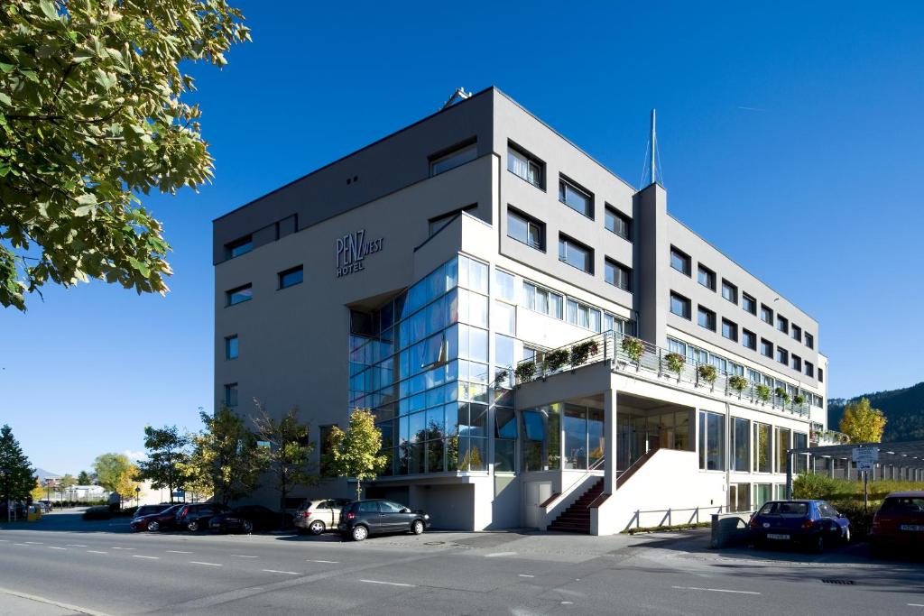 een groot wit gebouw met auto's geparkeerd op een parkeerplaats bij Hotel Penz West in Innsbruck