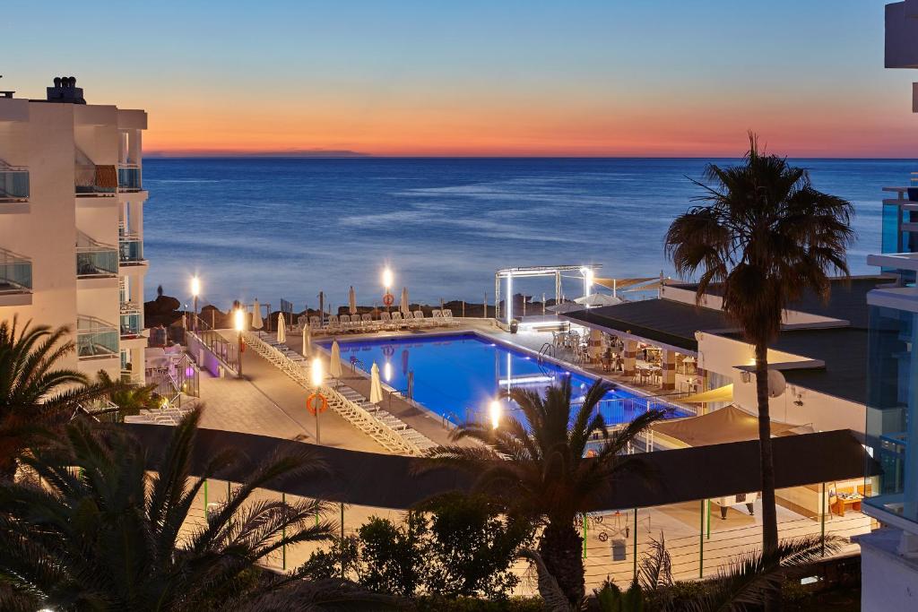 a view of a hotel with a pool and the ocean at Aparthotel Nereida in San Antonio Bay