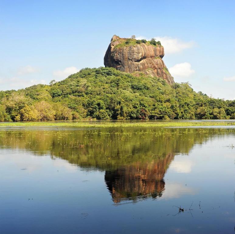 een rotsformatie weerspiegeld in het water van een meer bij Sunshine Resort & Spa Sigiriya in Sigiriya