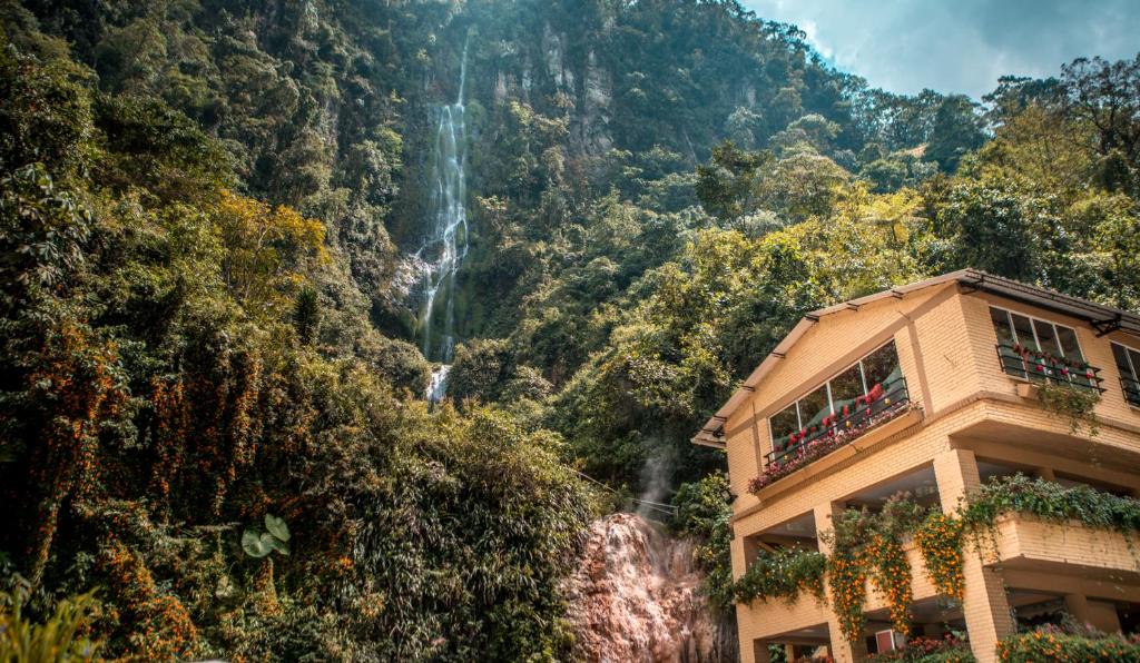a waterfall behind a building in front of a mountain at Termales Santa Rosa De Cabal in Santa Rosa de Cabal