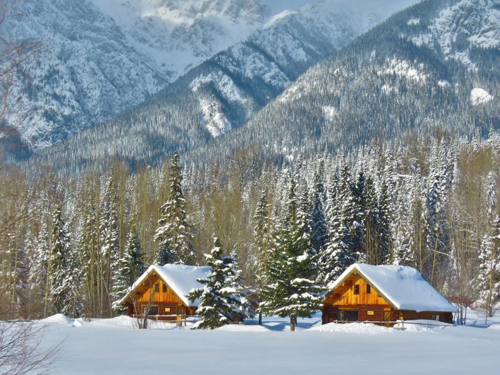two wooden cabins in the snow with mountains in the background at Rocky Ridge Resort-BC in Smithers