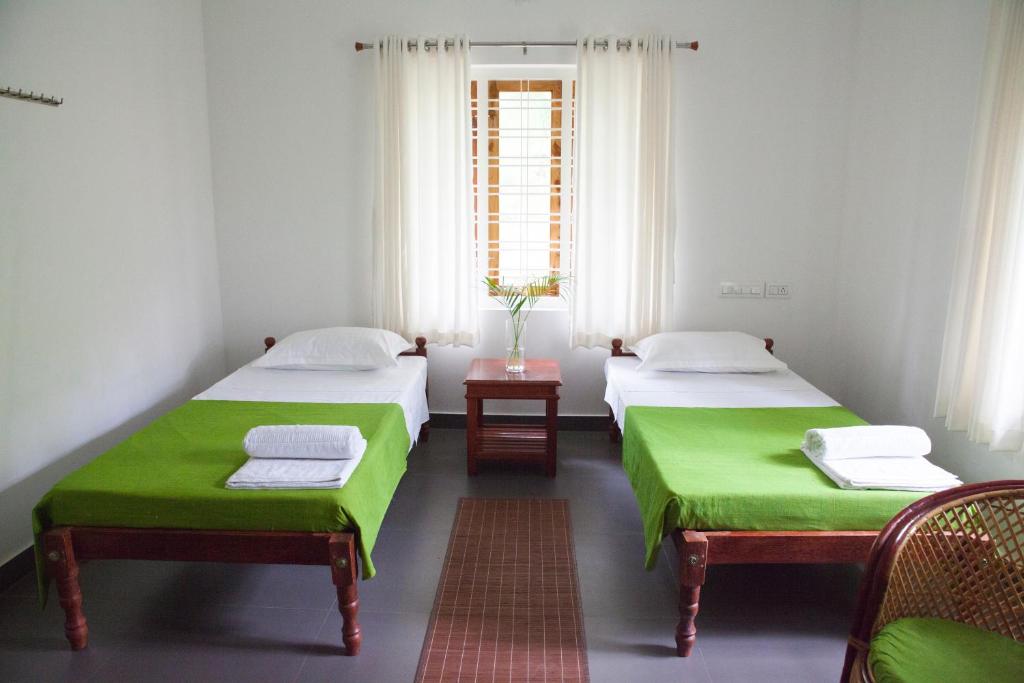two beds with green sheets in a room with a window at Mi Casa Tu Casa Homestay in Cochin