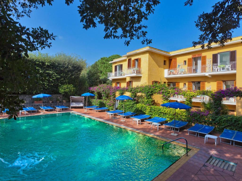 a pool with chairs and umbrellas in front of a hotel at Hotel Cleopatra in Ischia