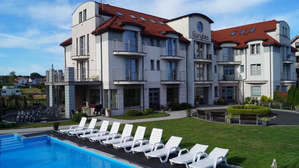 a hotel with a swimming pool and white chairs at Eurybia in Łeba