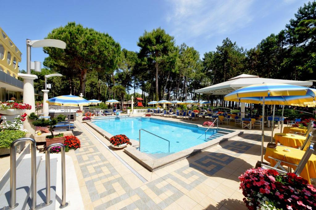 uma piscina com guarda-sóis, mesas e cadeiras em Hotel Colorado em Lignano Sabbiadoro