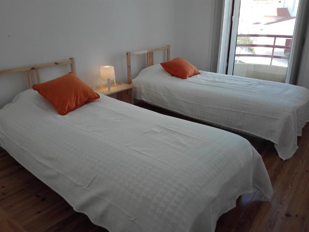 two beds with white sheets and orange pillows in a room at Largo da Igreja in Figueira da Foz