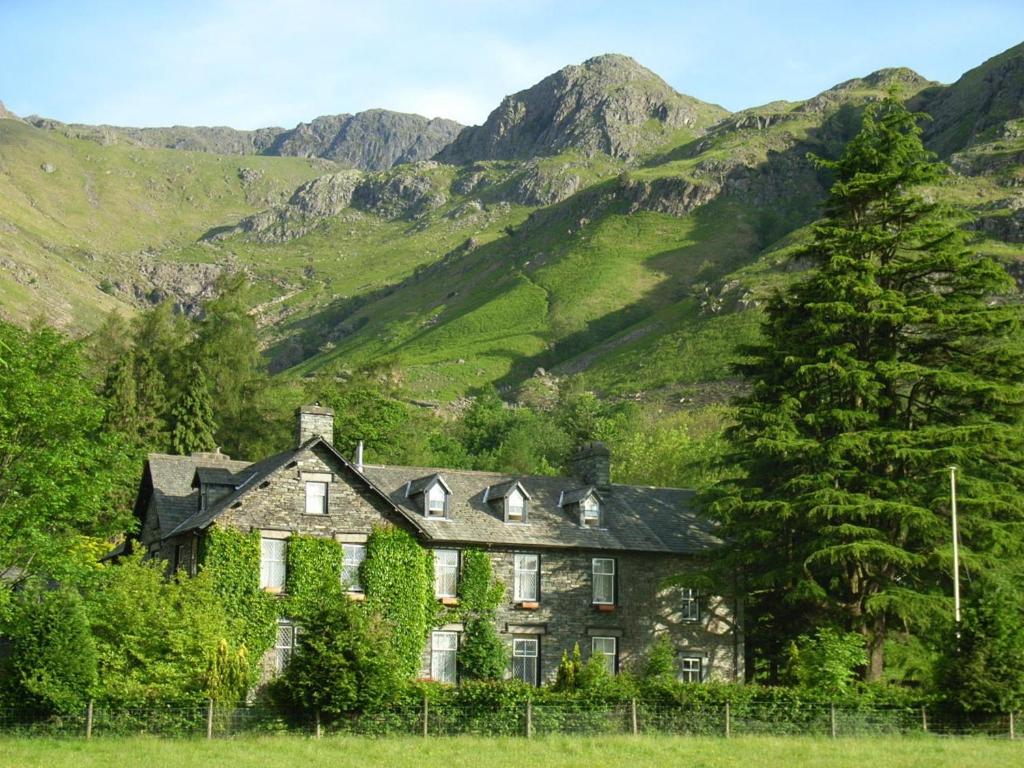 an old house in the mountains with a tree at New Dungeon Ghyll Hotel in Great Langdale