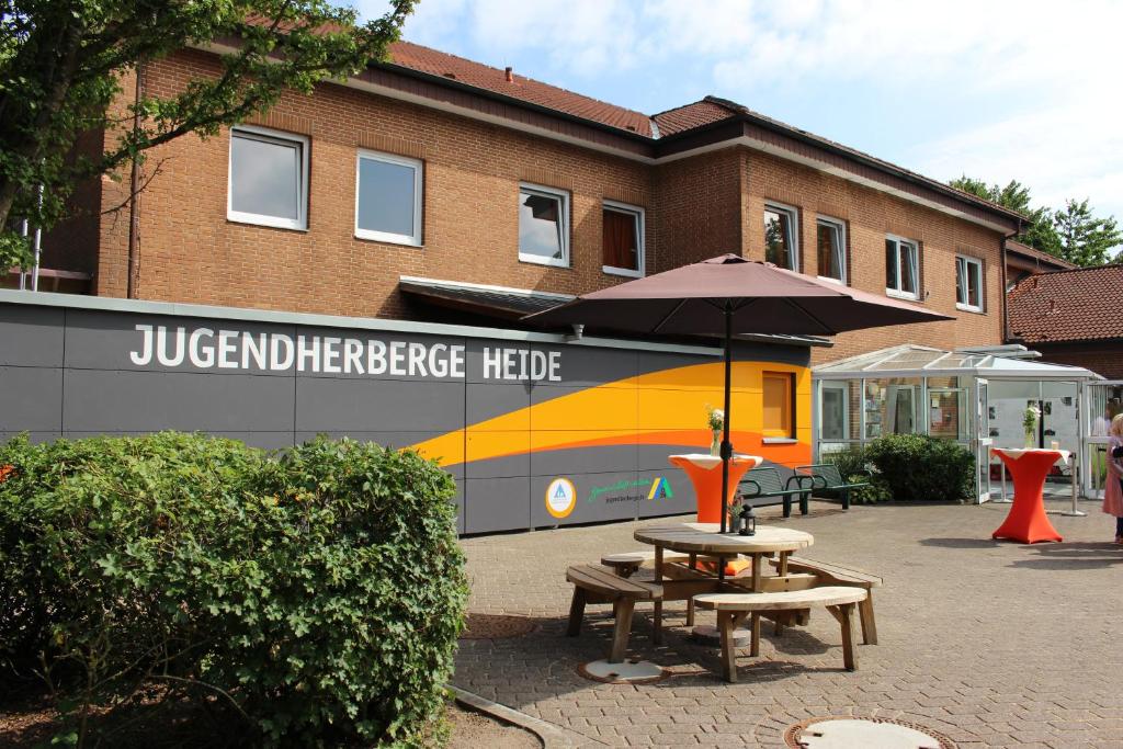 a picnic table with an umbrella in front of a building at Jugendherberge Heide in Heide