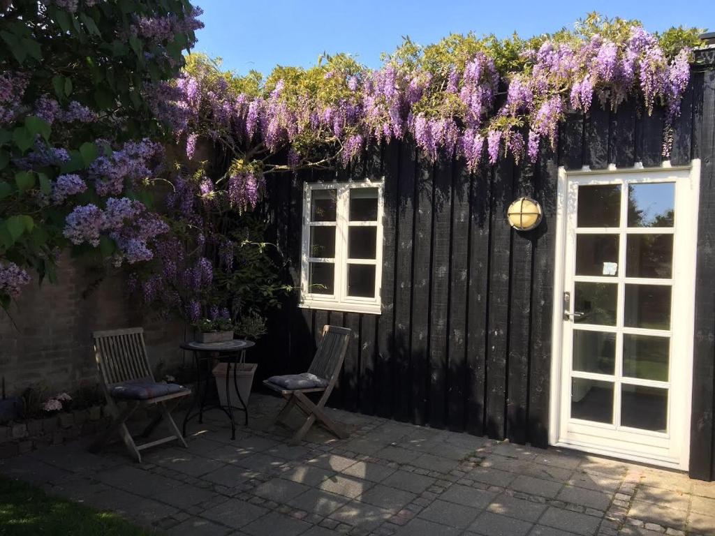 a patio with two chairs and a fence with purple flowers at Strandværelserne in Ebeltoft