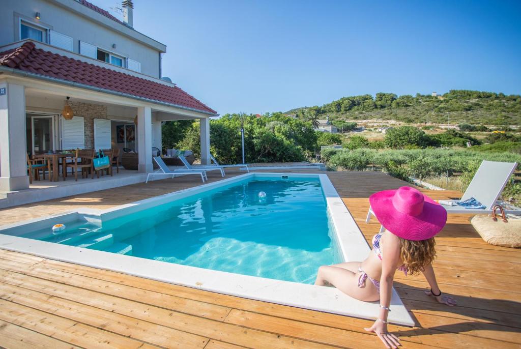a woman in a hat sitting on a deck next to a swimming pool at Villa Lastavica in Vis