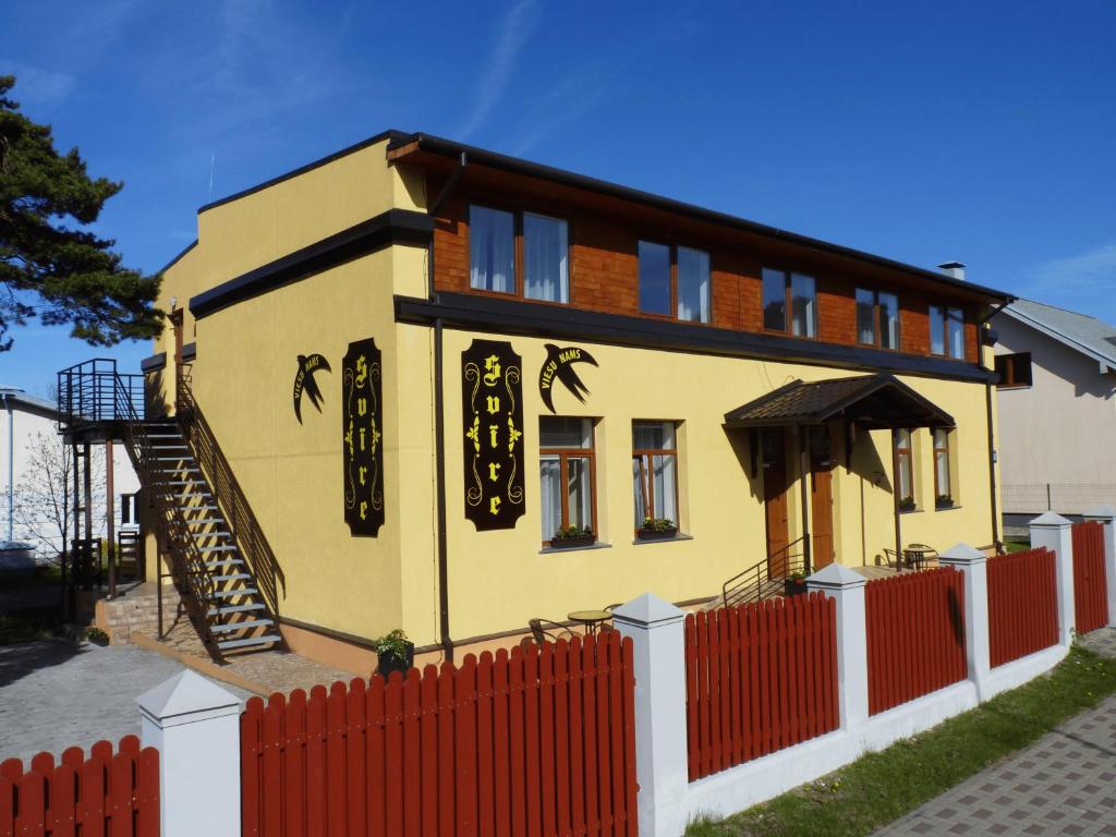 a small yellow house with a red fence at Viesu nams "Svīre-10" in Ventspils