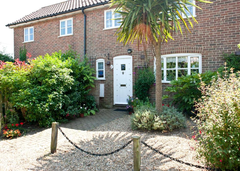 a brick house with a white door and a palm tree at Little Chequers in Friston