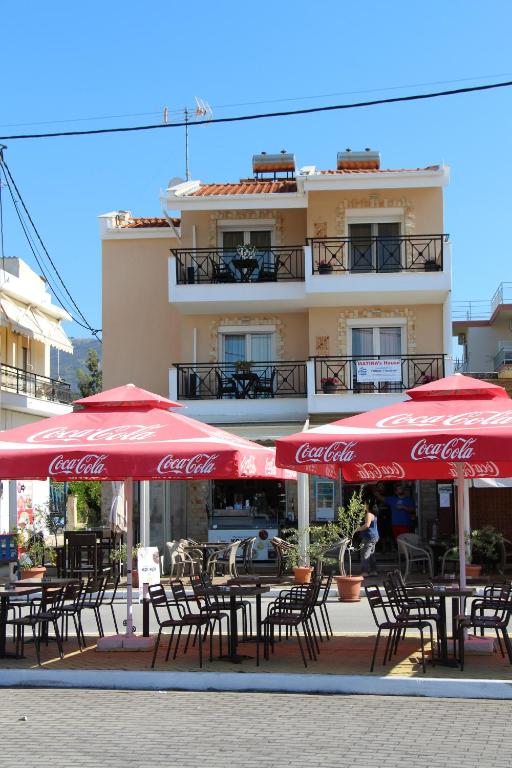 una cafetería al aire libre con sombrillas rojas, mesas y sillas en Matina's Apartments en Prinos