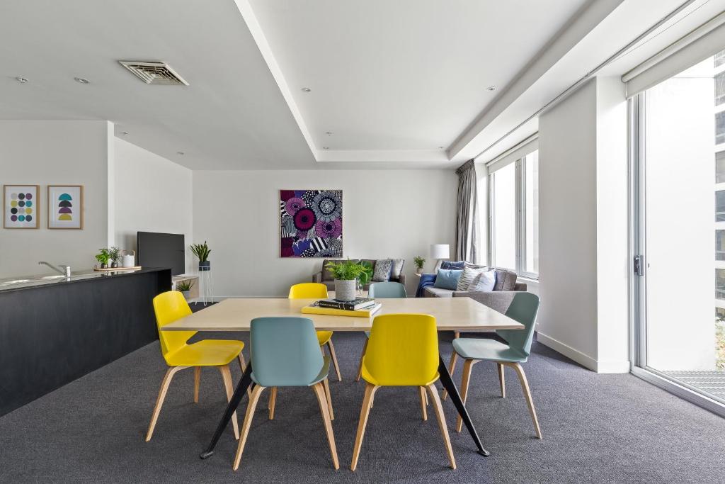 a dining room with a table and yellow chairs at Nook Melbourne Apartments : Collins Street - Melbourne CBD in Melbourne