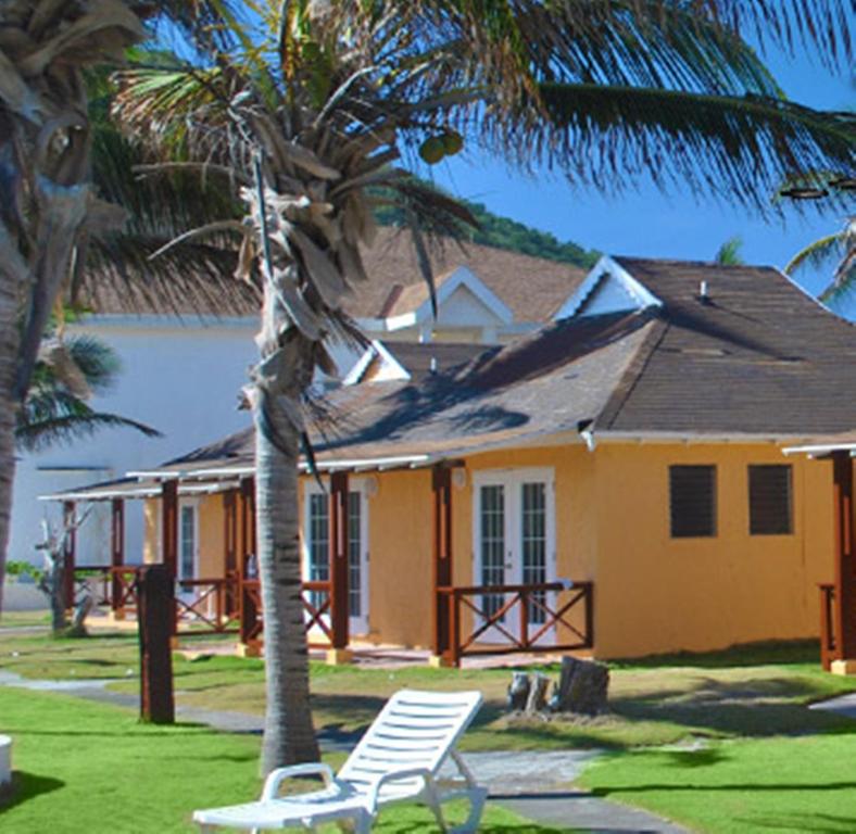 ein gelbes Haus mit einem Stuhl und einer Palme in der Unterkunft Sugar Bay Club in Frigate Bay