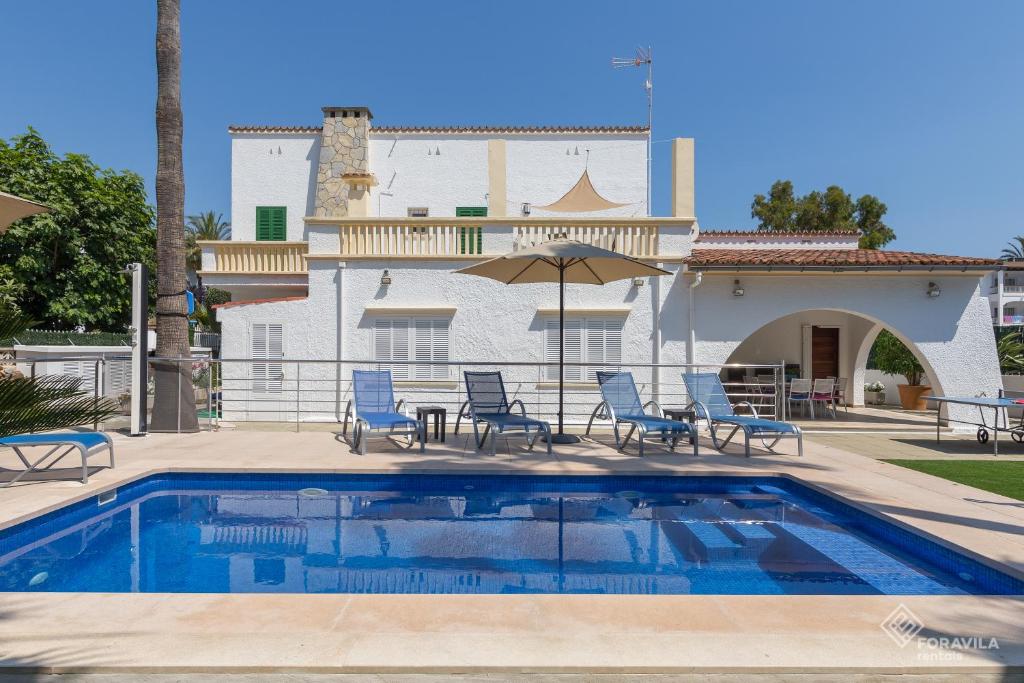 a pool in front of a house with chairs and an umbrella at Villa Sol in Alcudia