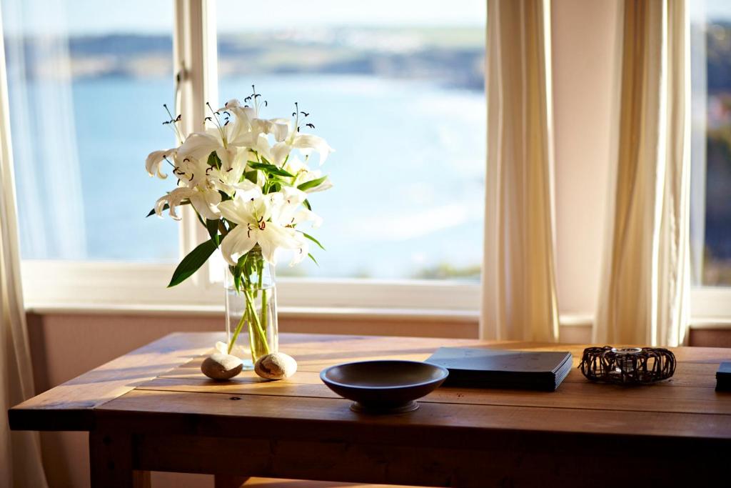 een vaas met witte bloemen op een tafel met een raam bij The Pad in Newquay