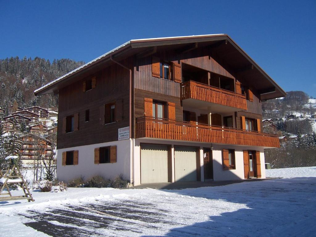 un grand bâtiment en bois avec un balcon dans la neige dans l'établissement le -charvin, au Grand-Bornand