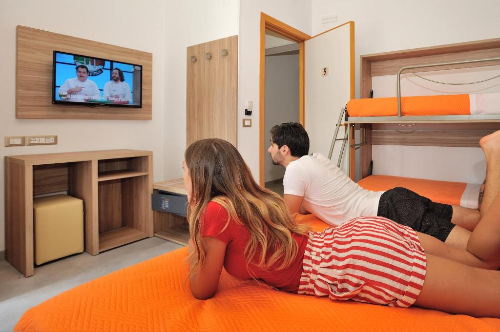 a man and a woman sitting on a bed watching tv at Hotel Lidia in Alba Adriatica