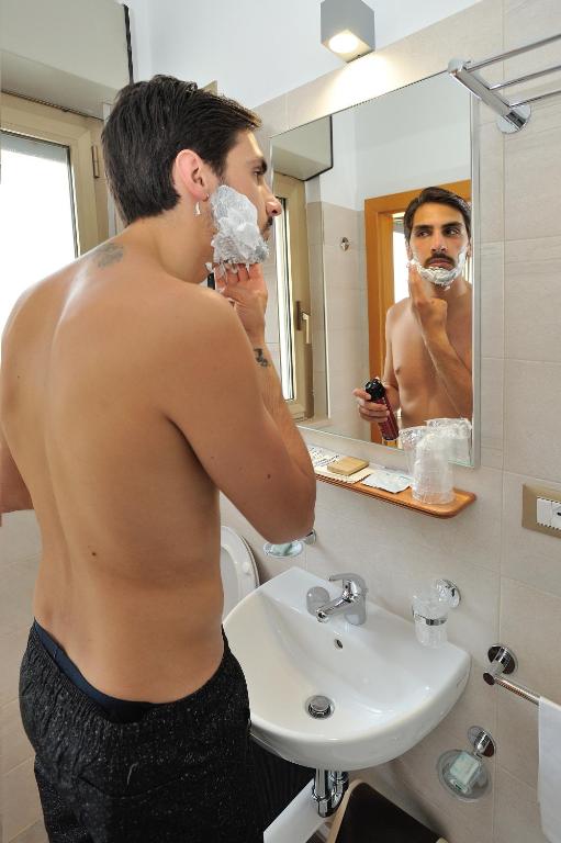 a shirtless man standing in a bathroom brushing his teeth at Hotel Lidia in Alba Adriatica