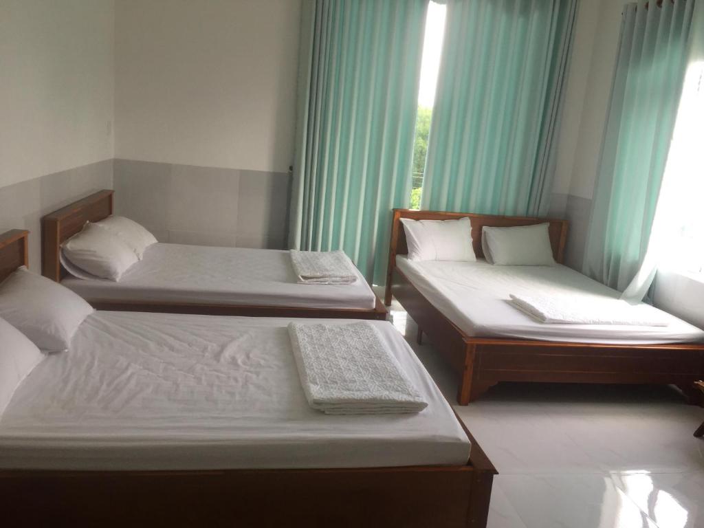 2 Betten in einem Zimmer mit grünen Vorhängen in der Unterkunft Motel Trần Nguyễn in La Gi