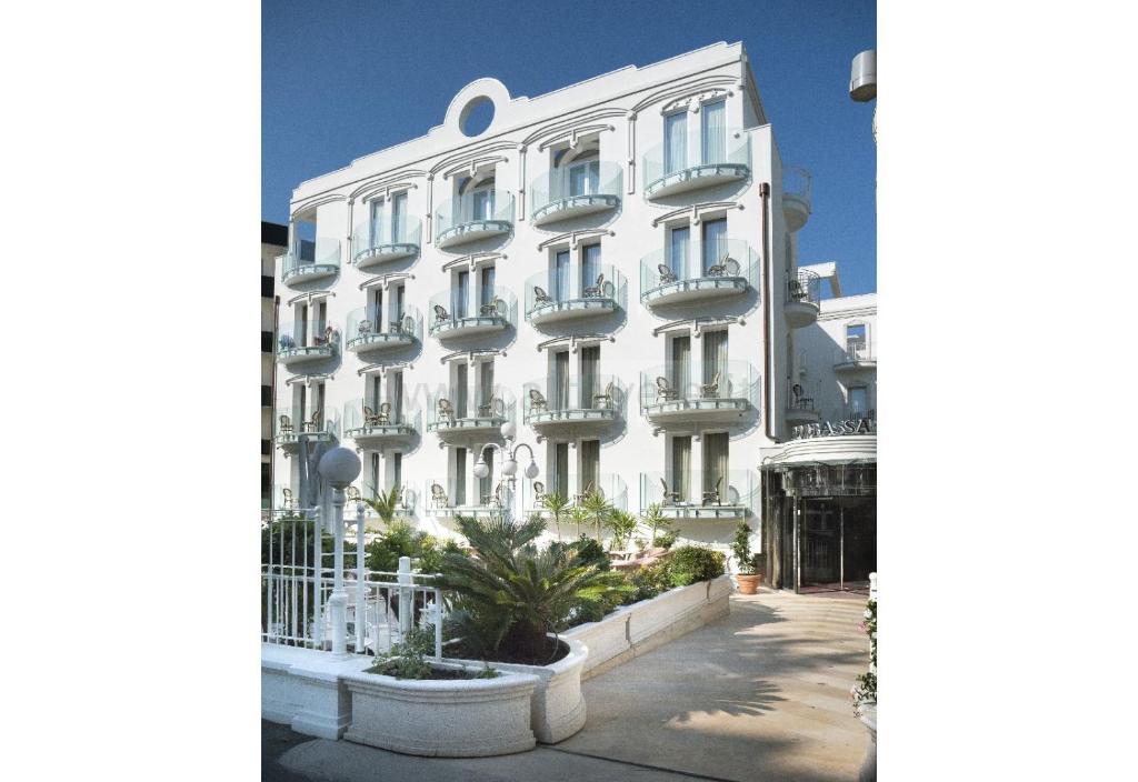 a large white building with a palm tree in front of it at Hotel Ambassador in Rimini
