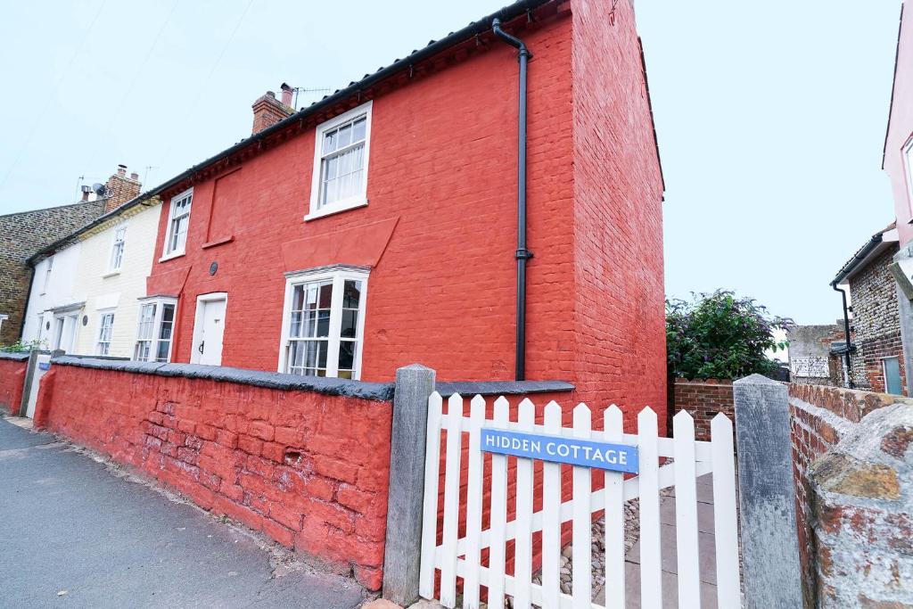 a red brick building with a white picket fence at Hidden Cottage, Aldeburgh in Aldeburgh