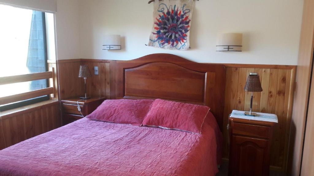a bedroom with a wooden bed with a pink bedspread at Departamento en Pucon in Pucón